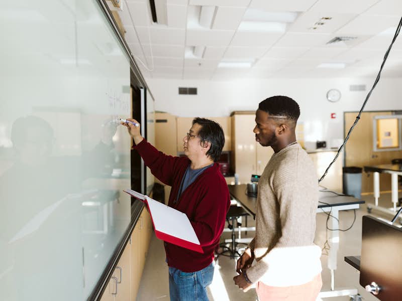 Gordon College student learns from his Physics professor as he writes on the whiteboard