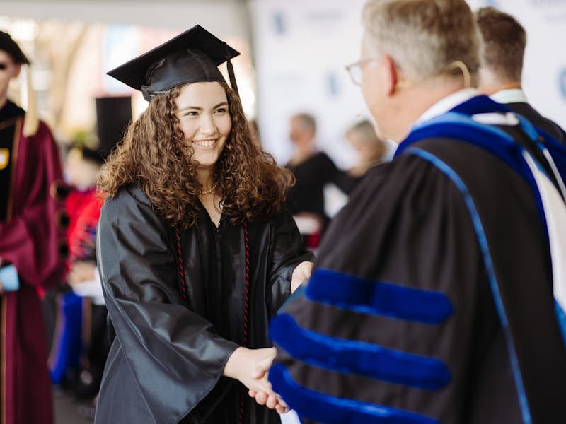 A graduating student shakes the president's hand and receives their diploma