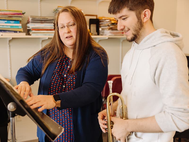 A music professor teaches her student how to play the trumpet