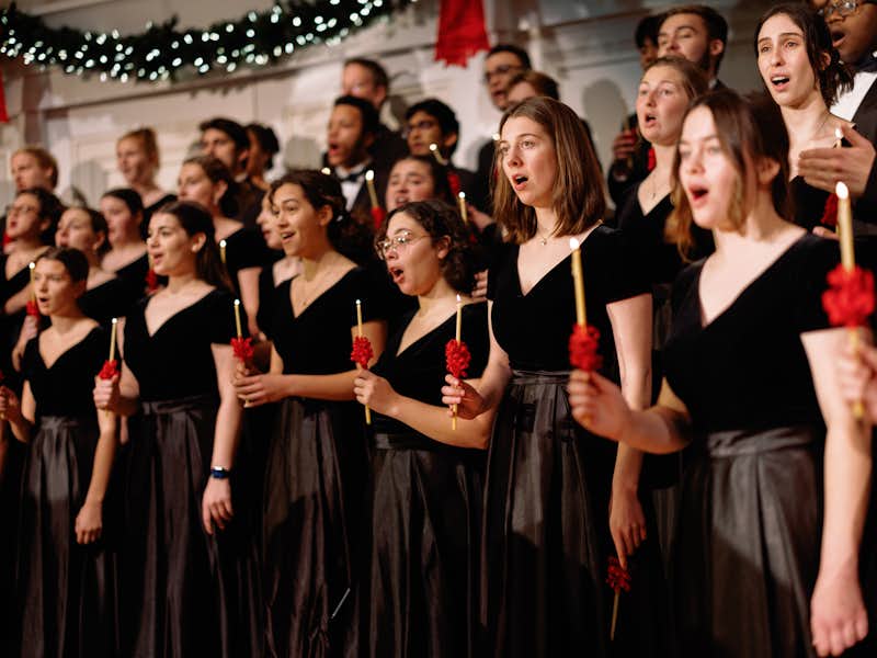 Students wearing black suits and dresses sing in a chorus in the Christmas Gala
