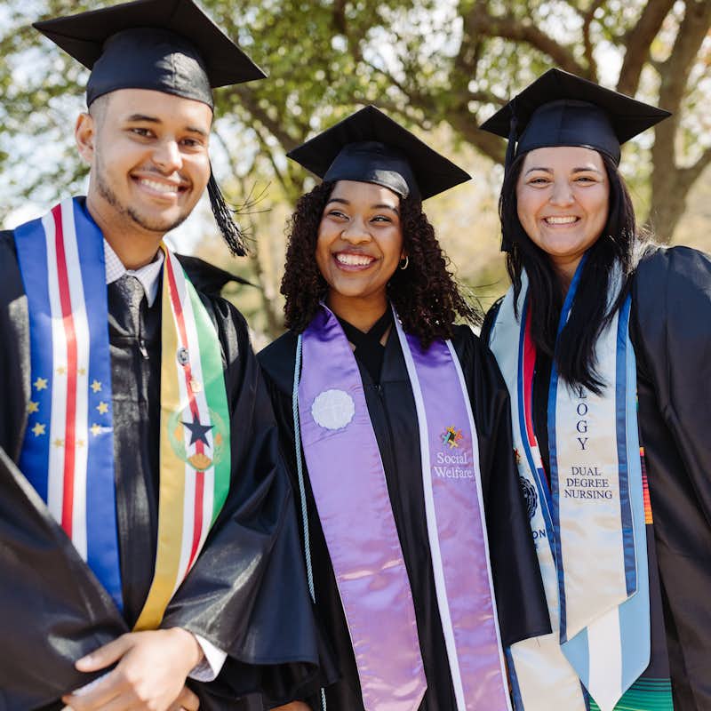 Three graduating students smile for a photo outdoors