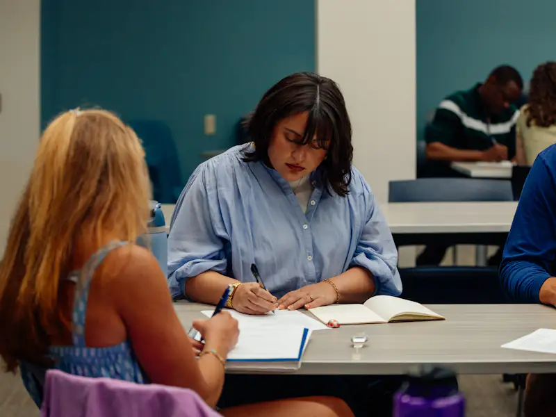 A woman sits at a table and takes notes in a class.