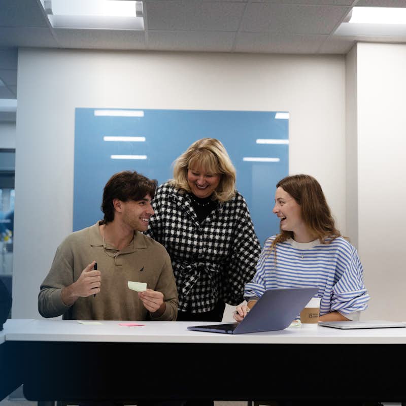 Two students work collaboratively with a professor at a table