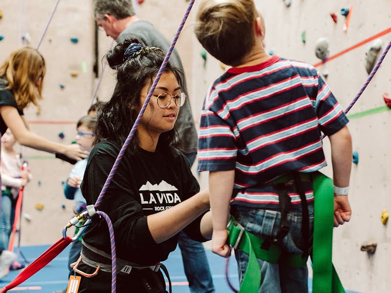 A Gordon College student assists a child in rock climbing