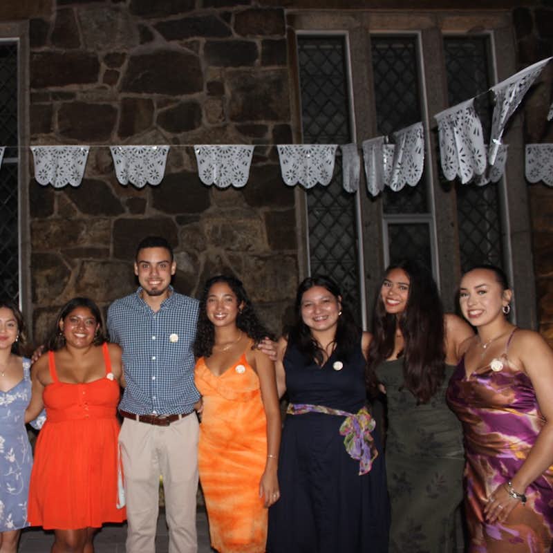 Group of students stand and pose for a photo at an outdoor nighttime celebration.