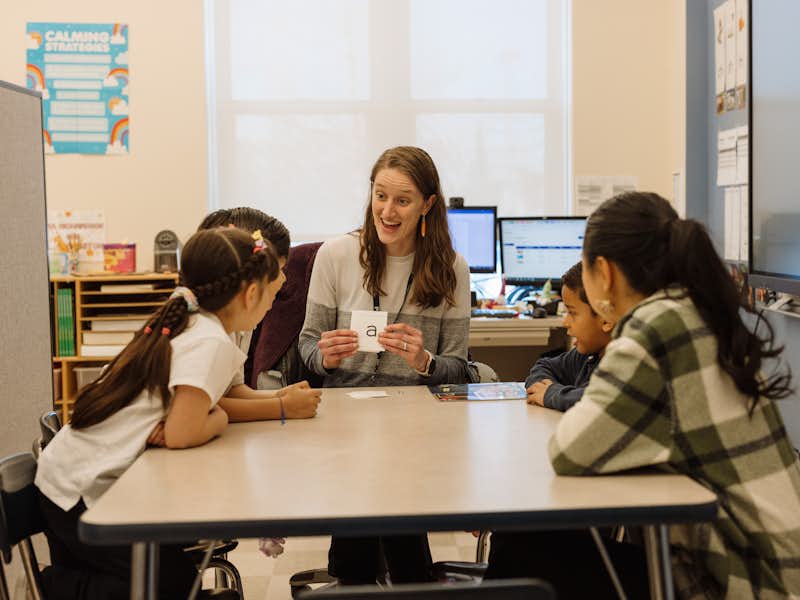 Student teacher works with a small group of students in a classroom.