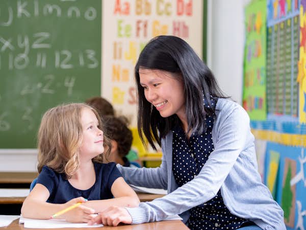 Elementary school teacher working with young student at a desk in class