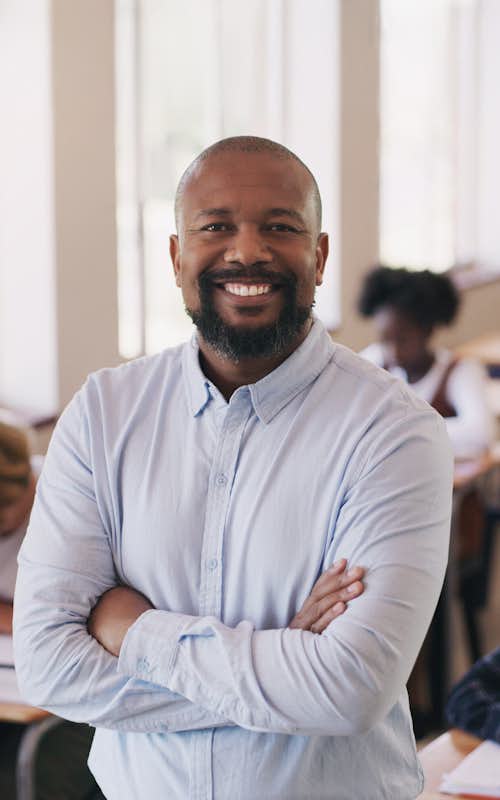 Male teacher stands in classroom with students working at desks behidn