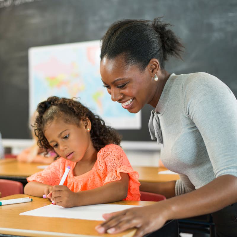 Female teacher works with young students at desks