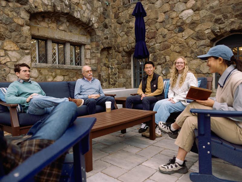 A linguistics class outside with students and the professor sitting outside on patio furniture.
