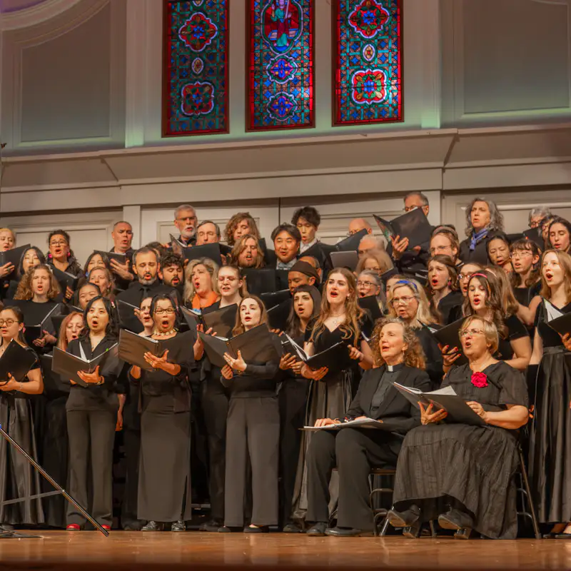 A choir of adults and college students wear matching black attire and sing on stage at the A. J. Gordon Memorial Chapel