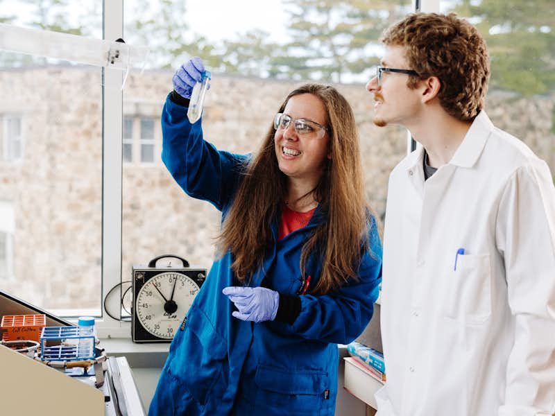 A student and chemistry professor examine a vial in a lab