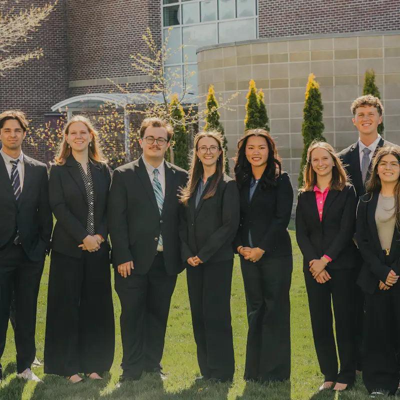 A group of college students wearing suits pose for a group photo outside