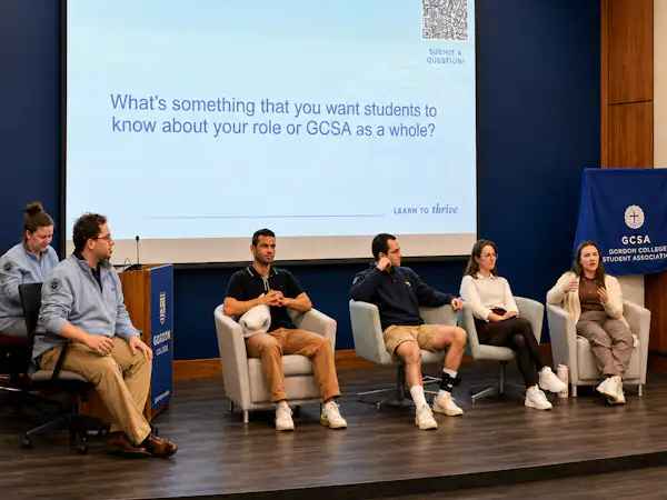 Five students sit on chairs on a stage in front of a presentation that reads "What's something that you want students to know about your role or GCSA as a whole?"