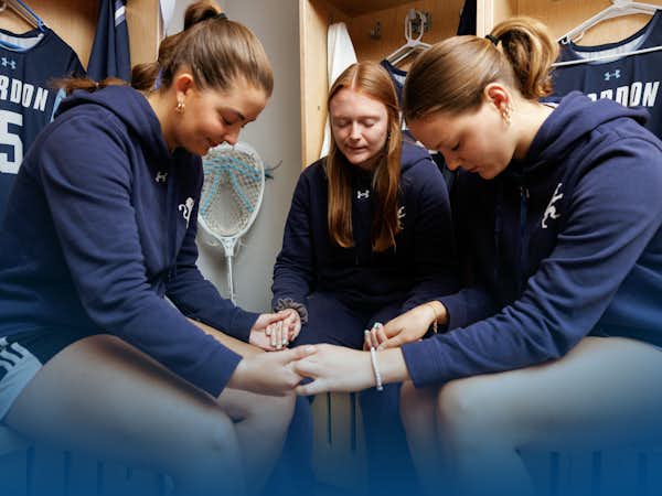 Three members of the women's lacrosse team hold hands to pray in the locker room