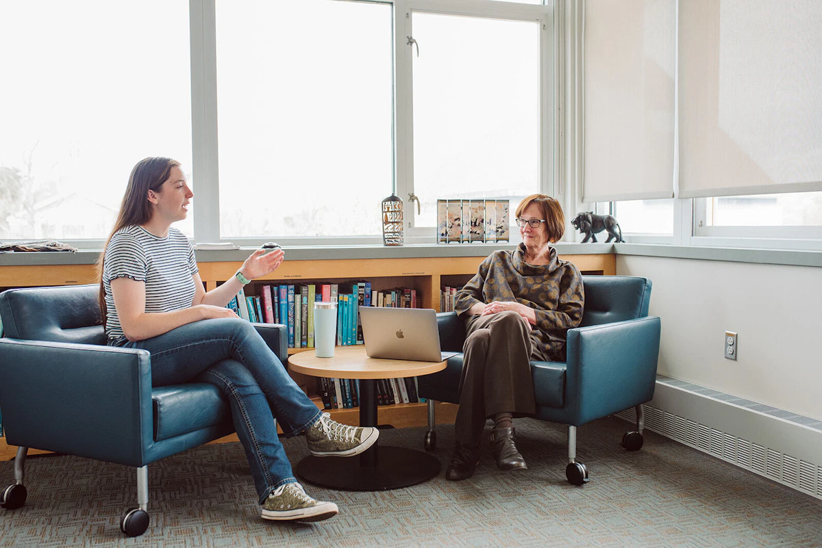 A psychologist and young woman speak with one another while sitting in chairs.