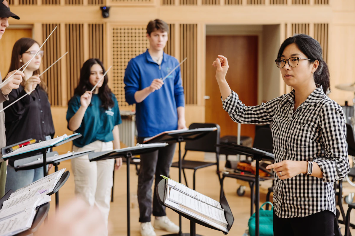 A woman leads a class of college students as they learn how to conduct.