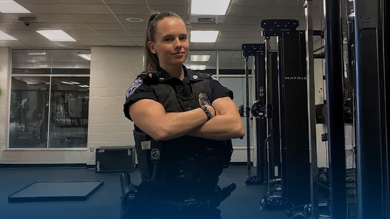Meredith Ketcher, female member of law enforcement, stands in uniform in the Gordon College Bennett Center weight room.