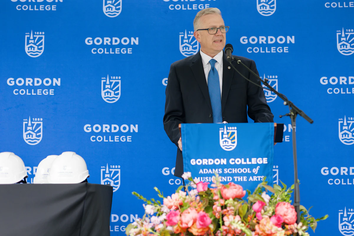President Michael Hammond addresses a crowd in front of a blue Gordon College backdrop.